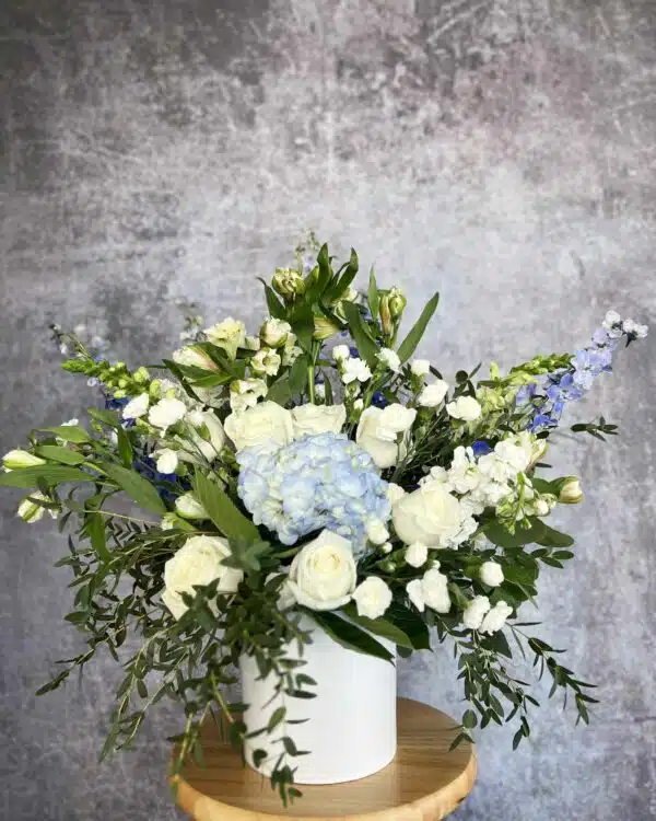 A "Sympathy Blue" flower arrangement featuring blue Hydrangeas, white Roses, and Baby's-breath in a white vase, available in Washington, NC.
