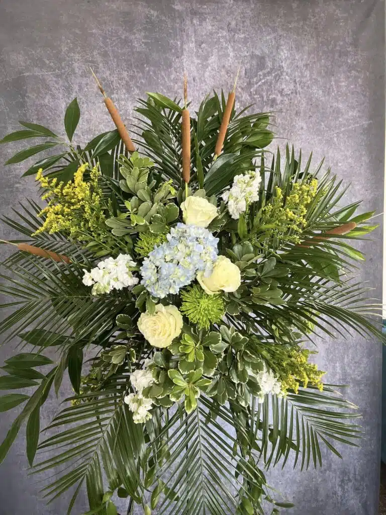 Standing spray for funeral or memorial service in Washington, NC, designed by Sun Moon and Bloom, with yellow Acacia, white flowers, and greenery.