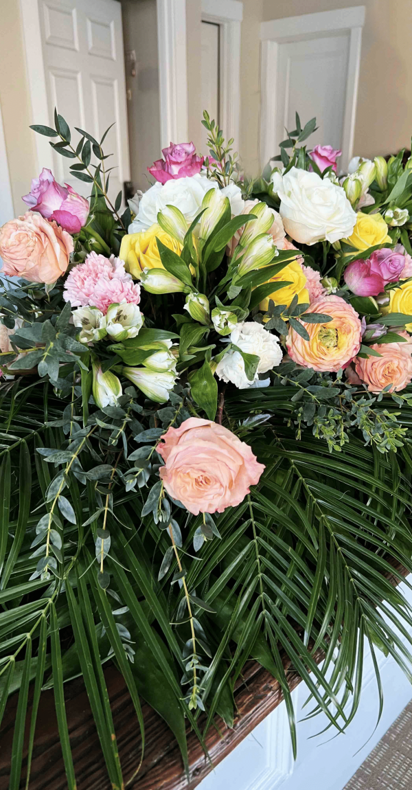 Beautiful casket spray with pink, yellow, and white flowers, designed by Sun Moon and Bloom, a local florist providing funeral flowers in Washington, NC.
